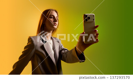 Business woman presenting smartphone toward camera isolated on yellow green gradient background Business woman presenting smartphone toward camera isolated on yellow green gradient background 137293570