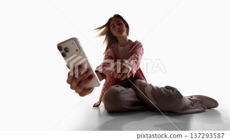 Young woman sitting on floor using smartphone isolated on white background. 137293587