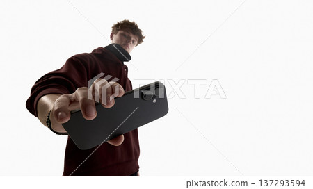 Low angle young man holding smartphone toward camera isolated on white background. Low angle young man holding smartphone toward camera isolated on white background. 137293594