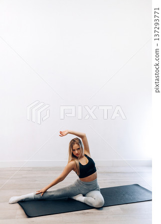 Young Woman Practices Seated Side Stretch Exercise In Indoor Gym Space Focusing On Health. Girl Stretching, Enjoying Fitness Training Yoga And Healthy Lifestyle. Young Woman Practices Seated Side Stretch Exercise In Indoor Gym Space Focusing On Health. Girl Stretching, Enjoying Fitness Training Yoga And Healthy Lifestyle. 137293771