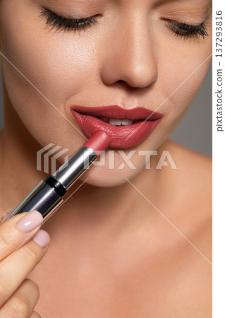 Woman applies lipstick with focus on her lips and skin in a skincare setting 137293816