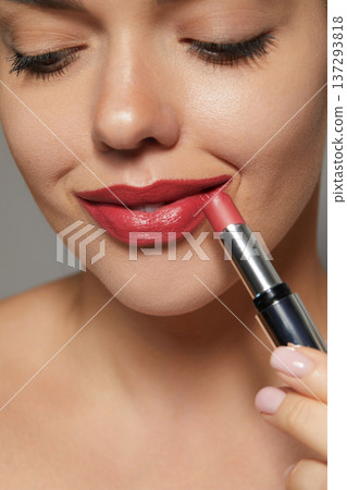 Woman applying lipstick while smiling in a skincare session at a beauty spa in bright lighting 137293818