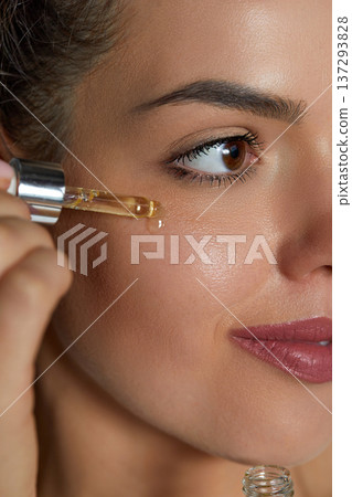 Skincare. Close up beauty portrait of a beautiful woman with glowing skin is applying a vitamin C skincare product with a pipette dropper. Serum. Moisturizing and nourishing. Skincare. Close up beauty portrait of a beautiful woman with glowing skin is applying a vitamin C skincare product with a pipette dropper. Serum. Moisturizing and nourishing. 137293828