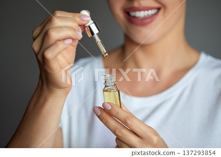 Skincare. Close up beauty portrait of a beautiful woman with glowing skin is applying a vitamin C skincare product with a pipette dropper. Serum. Moisturizing and nourishing 137293854