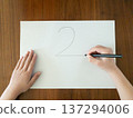 孩子用黑色鋼筆在白紙上寫數字2，正在木桌上學習。 137294006