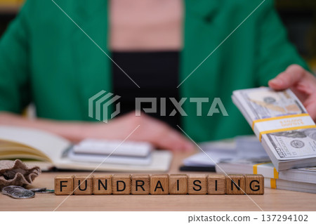 Creative fundraising efforts in a busy workspace with stacks of cash and wooden blocks Creative fundraising efforts in a busy workspace with stacks of cash and wooden blocks 137294102