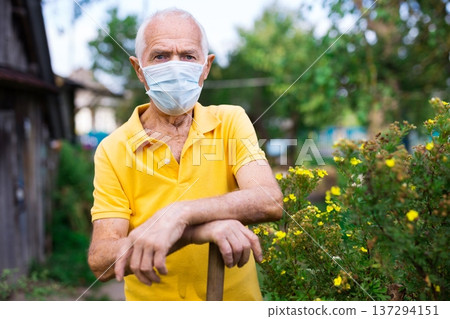 Portrait of adult farmer in protective mask with shovel on field Portrait of adult farmer in protective mask with shovel on field 137294151