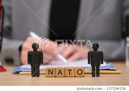 Figures stand by wooden blocks spelling NATO as a meeting occurs, highlighting partnership and unity in diplomacy and security discussions 137294156