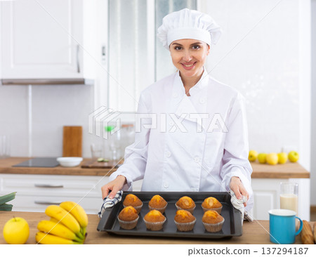 Portrait of positive female chef with just baked hot cupcakes Portrait of positive female chef with just baked hot cupcakes 137294187
