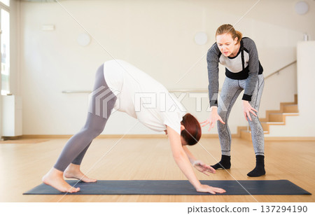 Pregnant woman practices yoga with an instructor. Downward Dog Pose or Adho Mukha Svanasana Pregnant woman practices yoga with an instructor. Downward Dog Pose or Adho Mukha Svanasana 137294190
