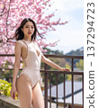 A woman in a white swimsuit stands on a terrace surrounded by cherry blossoms 137294723