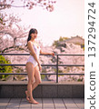 A Japanese woman in a swimsuit stands on an outdoor terrace surrounded by cherry blossoms 137294724