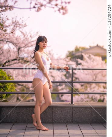 A Japanese woman in a swimsuit stands on an outdoor terrace surrounded by cherry blossoms 137294724