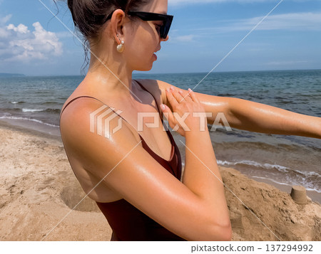 Attractive Woman Applying Suncream Sunscreen Lotion on Shoulder at Beach. Concept of sun protection, UV skincare and healthy lifestyle. 137294992