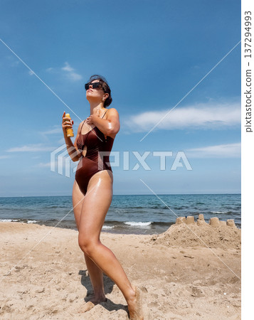 Beautiful Woman Using Suncream Sunscreen Lotion on Body at Beach. Concept of sun protection, UV skincare and healthy lifestyle. 137294993