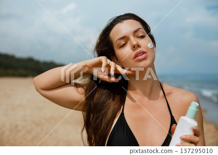 Beautiful woman applying sunscreen lotion on face at beach, summer skincare routine and sun protection concept with natural beauty and healthy skin 137295010
