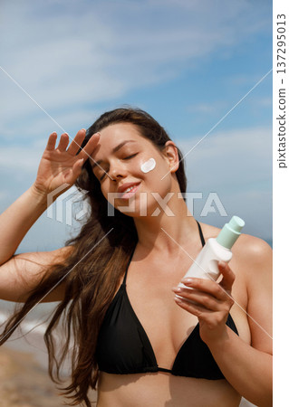 Beautiful woman enjoying skincare routine while applying sunscreen lotion on face at beach, beauty and sun protection concept with healthy lifestyle Beautiful woman enjoying skincare routine while applying sunscreen lotion on face at beach, beauty and sun protection concept with healthy lifestyle 137295013