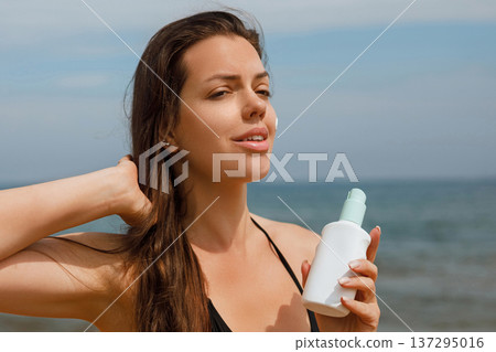 Relaxed woman enjoying sunlight while holding sunscreen lotion at beach, summer skincare and sun protection concept with calm lifestyle and glowing skin Relaxed woman enjoying sunlight while holding sunscreen lotion at beach, summer skincare and sun protection concept with calm lifestyle and glowing skin 137295016