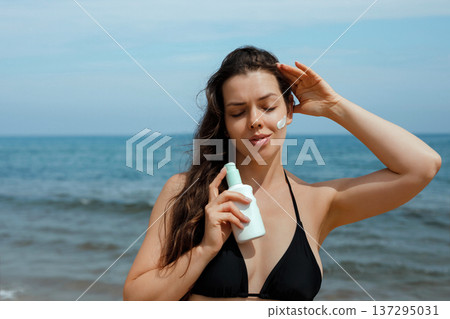 Smiling woman holding sunscreen suncream lotion and enjoying sunlight at beach, female using sunblock for healthy glowing skin Smiling woman holding sunscreen suncream lotion and enjoying sunlight at beach, female using sunblock for healthy glowing skin 137295031