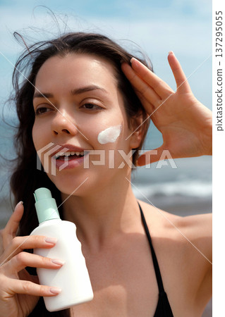 Close portrait of woman with sunscreen suncream lotion on face at beach, female using sunblock for skincare and UV protection Close portrait of woman with sunscreen suncream lotion on face at beach, female using sunblock for skincare and UV protection 137295055