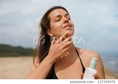 Young woman gently applying sunscreen lotion on cheek at beach under sunlight, facial skincare routine and sun protection concept with natural beauty 137295078