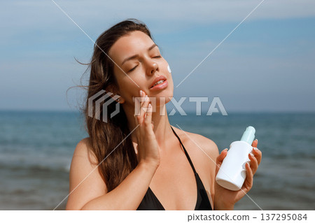 Close up of woman applying sunscreen on cheek using suncream lotion for skin protection at beach Close up of woman applying sunscreen on cheek using suncream lotion for skin protection at beach 137295084