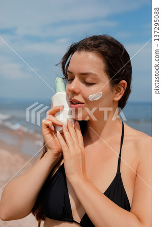 Woman gently applying sunscreen lotion on face at beach, skincare and sun protection concept 137295088
