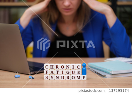 Struggling with chronic fatigue syndrome at a workspace with a laptop and stress visible in the air 137295174