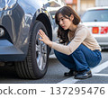 A Japanese woman anxiously checks the tires on her car in a parking lot. 137295476