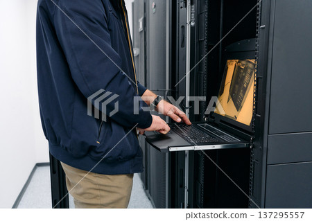IT technician working on laptop inside a server rack in a data center maintenance room 137295557