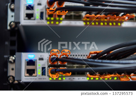 Close-up of network server rack with fiber optic cables and illuminated ports in data center Close-up of network server rack with fiber optic cables and illuminated ports in data center 137295573