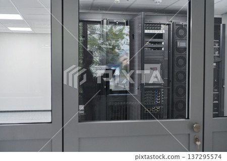 Data center server room seen through glass door with server racks and technician reflection 137295574