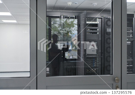 Technician inspecting servers through glass door in a modern data center server room Technician inspecting servers through glass door in a modern data center server room 137295576
