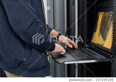 IT technician using a rack-mounted laptop to monitor servers during maintenance in a data center IT technician using a rack-mounted laptop to monitor servers during maintenance in a data center 137295589