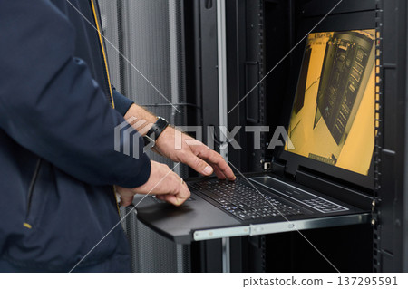 IT technician working on rack server console laptop in a data center server room monitoring equipment 137295591