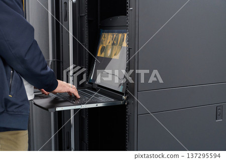 IT technician working on server rack console in data center with slide-out keyboard and monitor IT technician working on server rack console in data center with slide-out keyboard and monitor 137295594
