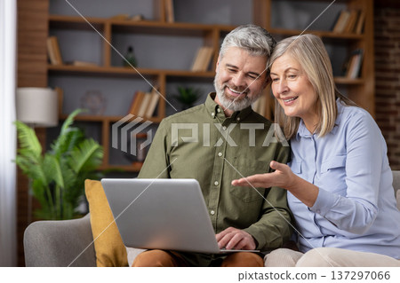 Senior couple relaxing on a sofa, smiling as they use a laptop together to browse the internet, video call, shop, and stay connected with family and modern technology Senior couple relaxing on a sofa, smiling as they use a laptop together to browse the internet, video call, shop, and stay connected with family and modern technology 137297066