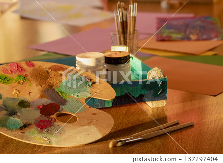 Painter's wooden palette covered in colorful paint swatches next to wooden art brushes Painter's wooden palette covered in colorful paint swatches next to wooden art brushes 137297404