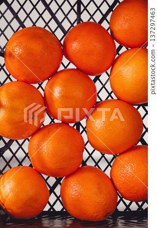 Fresh oranges in basket with black grid background. Bright orange fruits show natural texture and color. Slightly blurred edges add depth to image. Ideal for food, nutrition, or citrus-themed projects 137297463