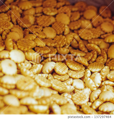 Round crackers fill a wooden container. Textured surfaces show crisp, baked edges. Warm lighting highlights their inviting appearance. Close-up view emphasizes snack appeal and texture 137297464