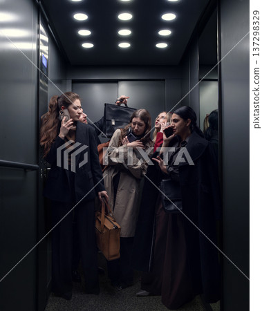 Group of businesswomen using smartphones while standing inside crowded office elevator. Group of businesswomen using smartphones while standing inside crowded office elevator. 137298329