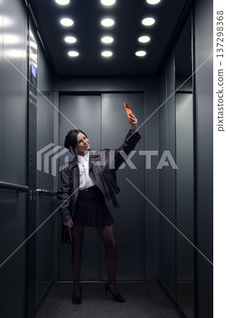 Young woman taking selfie with smartphone inside modern elevator Young woman taking selfie with smartphone inside modern elevator 137298368