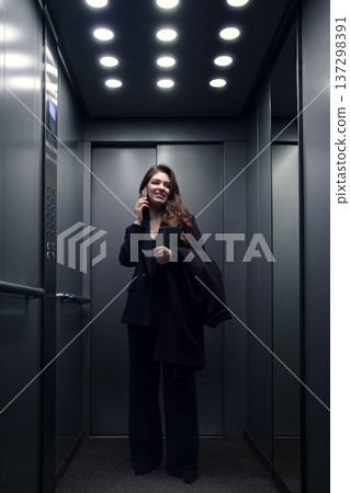 Businesswoman talking on smartphone while standing alone in modern office elevator 137298391