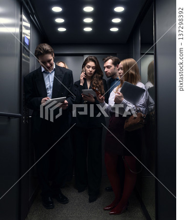 Group of business professionals using smartphones and tablets inside office elevator. Group of business professionals using smartphones and tablets inside office elevator. 137298392