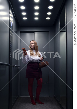 Businesswoman checking smartphone while standing alone in office elevator. Businesswoman checking smartphone while standing alone in office elevator. 137298394
