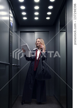 Businesswoman reading newspaper and talking on smartphone in modern office elevator. 137298396