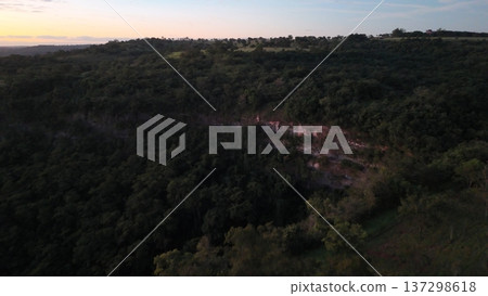 Cassilandia, Mato Grosso do Sul, Brazil - 04 05 2024. Drone aerial view of Cachoeira do Socorro waterfall flowing over a rocky cliff surrounded by dense forest vegetation during early morning light. Cassilandia, Mato Grosso do Sul, Brazil - 04 05 2024. Drone aerial view of Cachoeira do Socorro waterfall flowing over a rocky cliff surrounded by dense forest vegetation during early morning light. 137298618