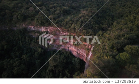 Cassilandia, Mato Grosso do Sul, Brazil - 04 05 2024. Drone aerial view of Cachoeira do Socorro waterfall flowing over a rocky cliff surrounded by dense forest vegetation during early morning light. Cassilandia, Mato Grosso do Sul, Brazil - 04 05 2024. Drone aerial view of Cachoeira do Socorro waterfall flowing over a rocky cliff surrounded by dense forest vegetation during early morning light. 137298619