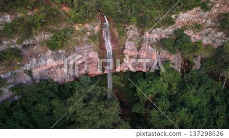 Cassilandia, Mato Grosso do Sul, Brazil - 04 05 2024. Drone aerial view of Cachoeira do Socorro waterfall flowing over a rocky cliff surrounded by dense forest vegetation during early morning light. Cassilandia, Mato Grosso do Sul, Brazil - 04 05 2024. Drone aerial view of Cachoeira do Socorro waterfall flowing over a rocky cliff surrounded by dense forest vegetation during early morning light. 137298626