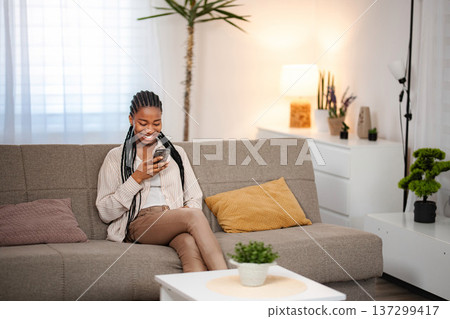 Young adult woman relaxing on sofa using smartphone Young adult woman relaxing on sofa using smartphone 137299417